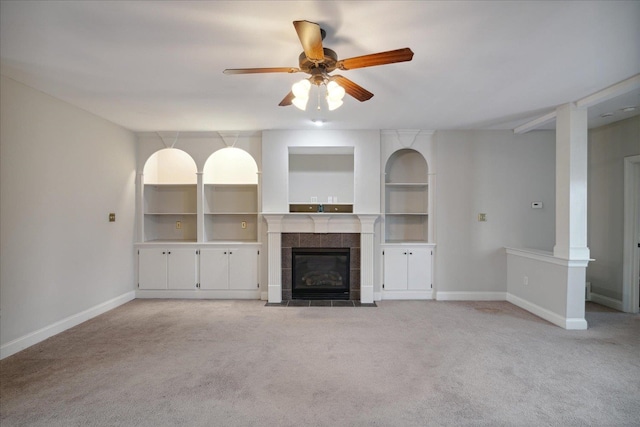 unfurnished living room featuring built in shelves, ceiling fan, light carpet, and a tiled fireplace