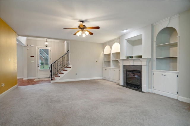 unfurnished living room featuring built in shelves, a fireplace, light carpet, and ceiling fan