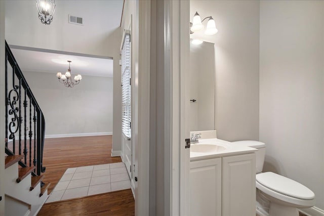 bathroom featuring wood-type flooring, vanity, toilet, and an inviting chandelier