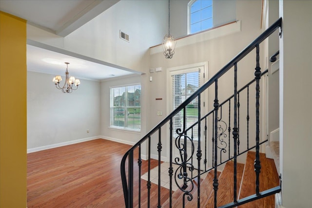 stairs featuring wood-type flooring, a notable chandelier, ornamental molding, and plenty of natural light