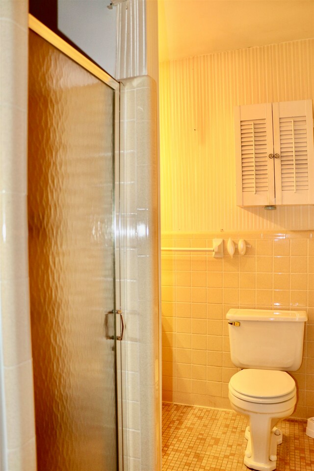 bathroom featuring tile patterned flooring, toilet, a wainscoted wall, tile walls, and a stall shower