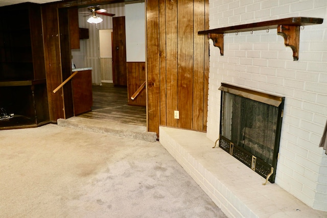 unfurnished living room with carpet floors, wooden walls, a fireplace, and a ceiling fan