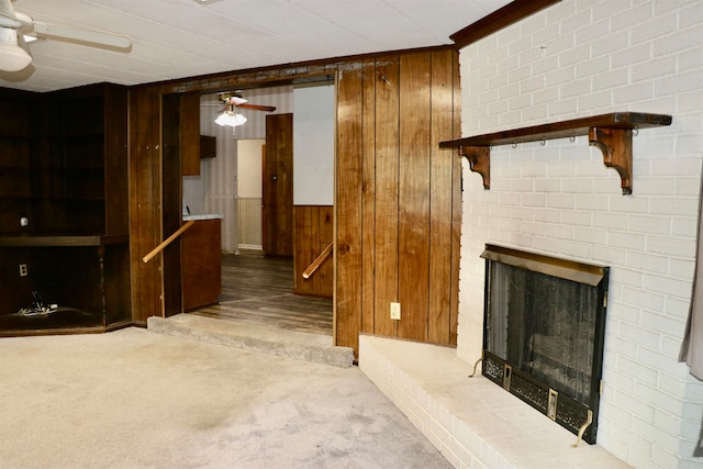 unfurnished living room featuring wooden walls, ceiling fan, a fireplace, and carpet flooring