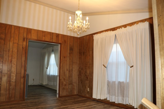 unfurnished room featuring a notable chandelier, dark wood finished floors, and wooden walls