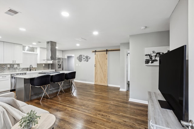 kitchen with wall chimney exhaust hood, a barn door, white cabinetry, dark hardwood / wood-style floors, and a kitchen island