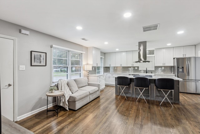 kitchen with a breakfast bar area, white cabinets, stainless steel fridge, and wall chimney exhaust hood