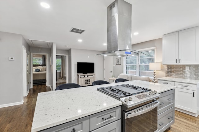 kitchen with gas stove, island range hood, white cabinetry, and plenty of natural light