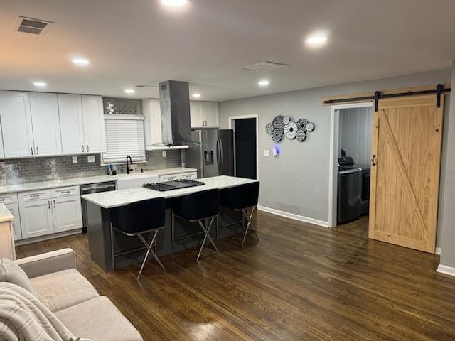 kitchen with white cabinetry, a kitchen island, appliances with stainless steel finishes, wall chimney exhaust hood, and dark hardwood / wood-style floors