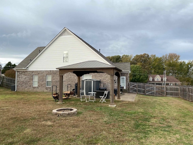 rear view of house with a fire pit, a gazebo, brick siding, and a fenced backyard