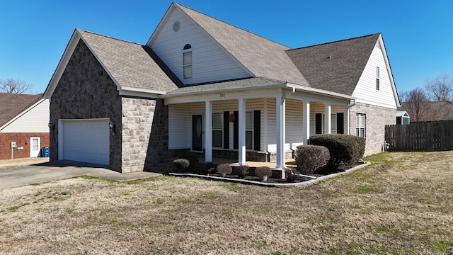 view of front of home featuring covered porch, a shingled roof, stone siding, driveway, and a front yard