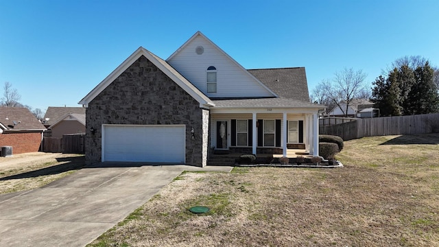 view of front facade with covered porch, concrete driveway, a front yard, fence, and stone siding