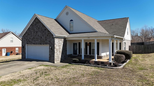 view of front of property featuring a shingled roof, concrete driveway, stone siding, a porch, and a front lawn