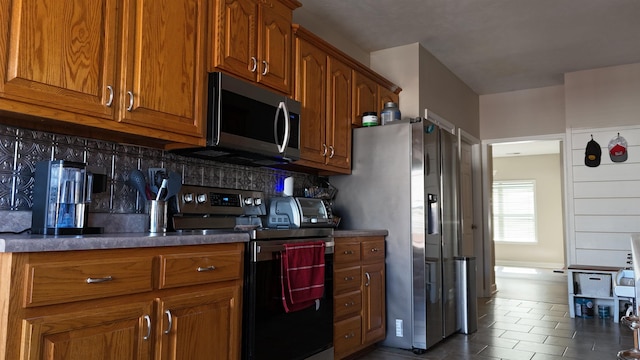 kitchen with dark countertops, tasteful backsplash, appliances with stainless steel finishes, and brown cabinetry