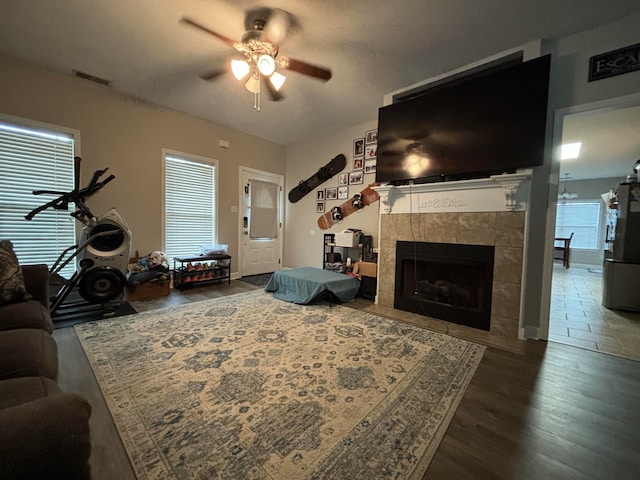 living room featuring a ceiling fan, visible vents, dark wood-type flooring, and a tile fireplace