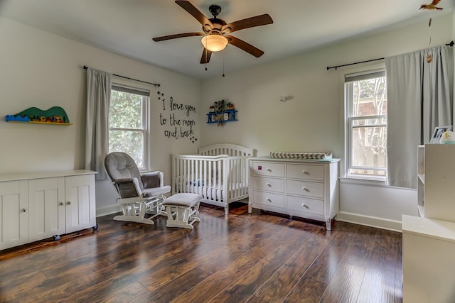 bedroom featuring dark wood-type flooring, multiple windows, a nursery area, and ceiling fan