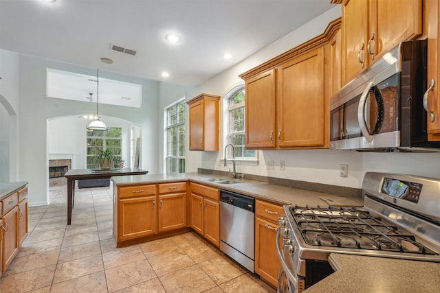 kitchen featuring stainless steel appliances, sink, kitchen peninsula, a fireplace, and pendant lighting