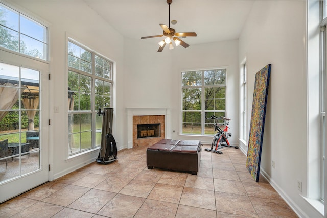 tiled living room with a tiled fireplace, a healthy amount of sunlight, a high ceiling, and ceiling fan