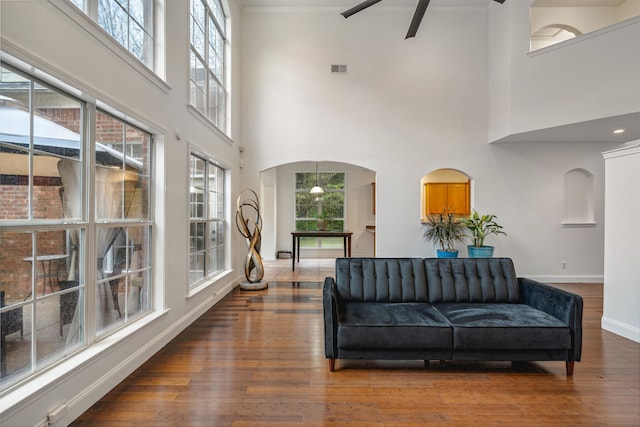 living room with dark wood-type flooring, a towering ceiling, and plenty of natural light