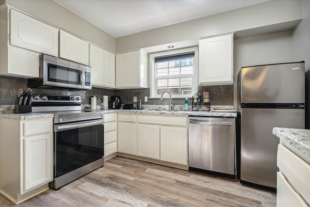 kitchen featuring tasteful backsplash, appliances with stainless steel finishes, sink, light hardwood / wood-style floors, and white cabinets