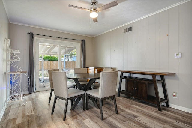 dining area with ornamental molding, wooden walls, hardwood / wood-style flooring, and ceiling fan