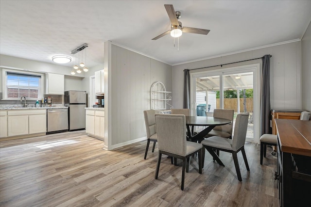 dining area featuring light hardwood / wood-style floors, wood walls, sink, ceiling fan, and crown molding