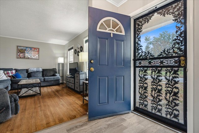 foyer featuring wood-type flooring, a textured ceiling, and crown molding