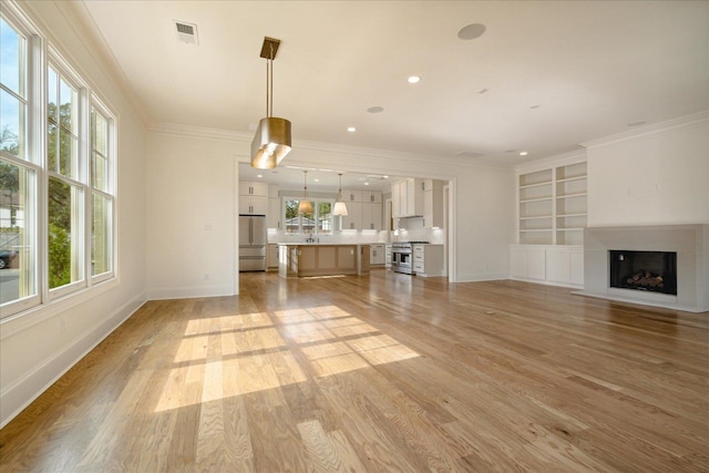 unfurnished living room featuring built in shelves, light wood-type flooring, and crown molding