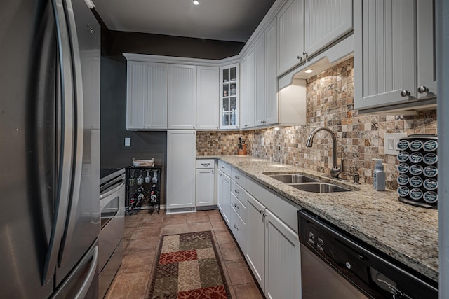 kitchen with stainless steel appliances, white cabinetry, sink, light stone countertops, and decorative backsplash