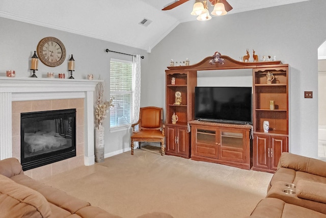 carpeted living room with ornamental molding, a tiled fireplace, lofted ceiling, and ceiling fan