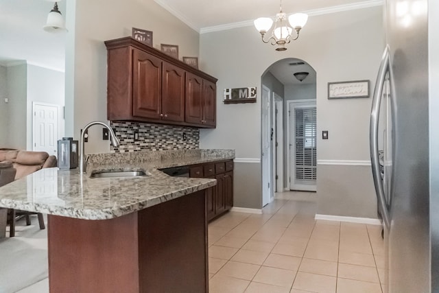 kitchen featuring light stone counters, hanging light fixtures, sink, tasteful backsplash, and stainless steel refrigerator