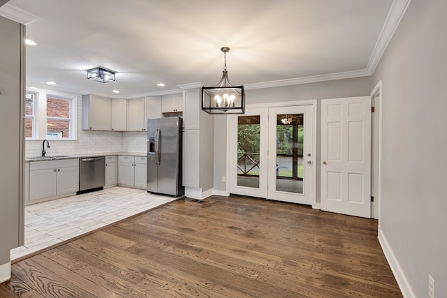 kitchen with tasteful backsplash, crown molding, hanging light fixtures, appliances with stainless steel finishes, and hardwood / wood-style flooring