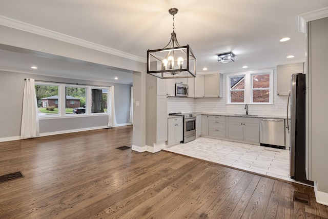 kitchen with stainless steel appliances, tasteful backsplash, ornamental molding, decorative light fixtures, and light wood-type flooring