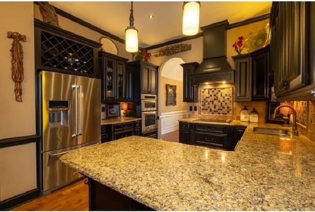 kitchen featuring stainless steel appliances, sink, custom exhaust hood, crown molding, and decorative light fixtures