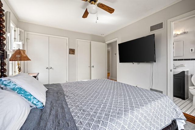 bedroom featuring connected bathroom, two closets, ceiling fan, and crown molding