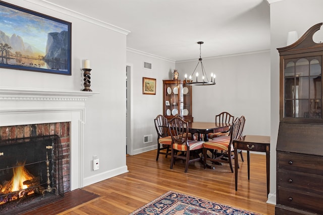 dining space featuring a brick fireplace, hardwood / wood-style floors, crown molding, and an inviting chandelier