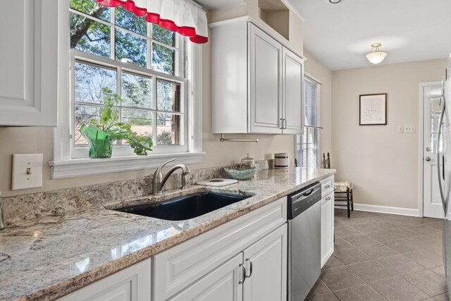 kitchen featuring white cabinets, stainless steel dishwasher, light stone counters, and sink