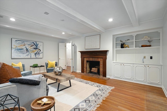 living room featuring built in shelves, ornamental molding, beam ceiling, a fireplace, and light wood-type flooring