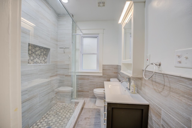 bathroom with vanity, toilet, tile walls, and a tile shower