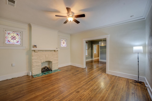 unfurnished living room with hardwood / wood-style floors, ceiling fan, a stone fireplace, and ornamental molding