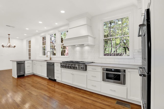 kitchen featuring hardwood / wood-style floors, kitchen peninsula, hanging light fixtures, white cabinetry, and appliances with stainless steel finishes