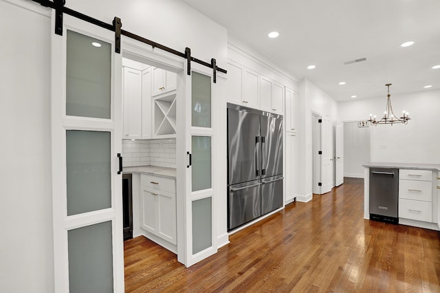 kitchen featuring dark hardwood / wood-style flooring, white cabinets, a barn door, backsplash, and stainless steel fridge