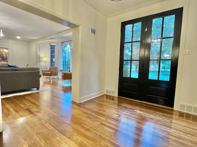 foyer with ornamental molding, light hardwood / wood-style floors, french doors, and a healthy amount of sunlight