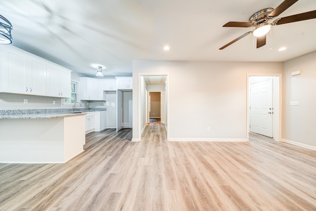 kitchen with light hardwood / wood-style floors, sink, ceiling fan, light stone countertops, and white cabinetry