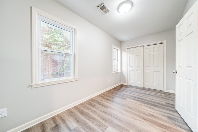 unfurnished bedroom featuring a closet, multiple windows, and light hardwood / wood-style floors