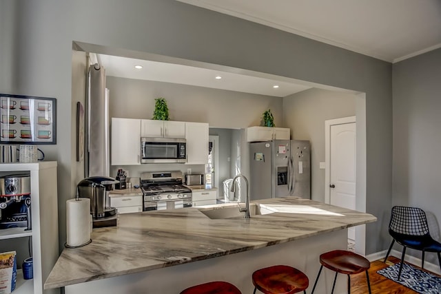 kitchen with appliances with stainless steel finishes, stone counters, sink, hardwood / wood-style flooring, and a breakfast bar