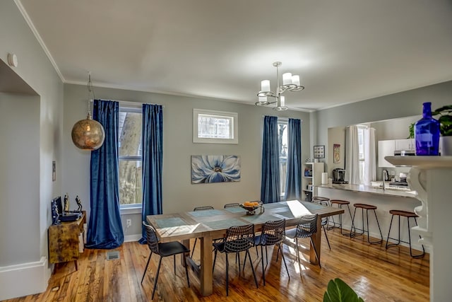 dining area with ornamental molding, light hardwood / wood-style floors, sink, and an inviting chandelier