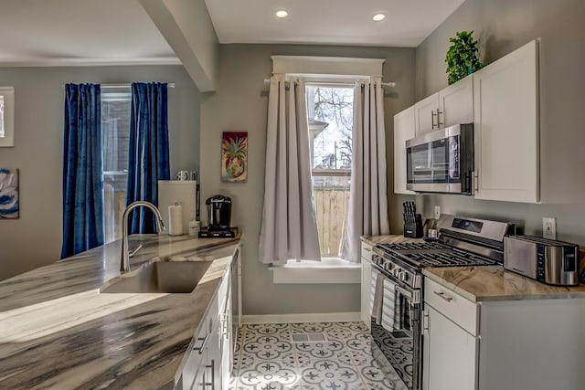 kitchen featuring stainless steel appliances, light tile patterned floors, light stone countertops, sink, and white cabinets