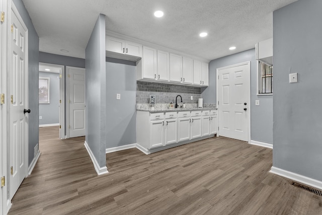 kitchen featuring light stone countertops, light hardwood / wood-style floors, white cabinetry, and decorative backsplash