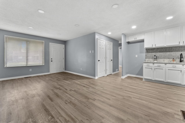 kitchen with light stone counters, decorative backsplash, a textured ceiling, white cabinetry, and light wood-type flooring