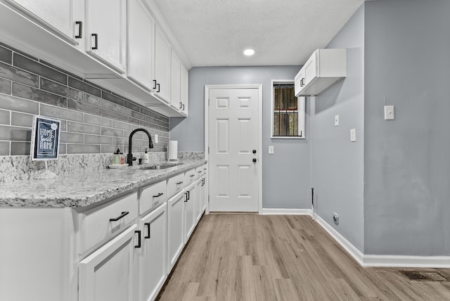 kitchen featuring white cabinets, light stone countertops, sink, and light hardwood / wood-style flooring